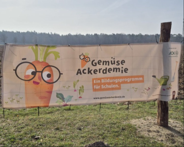 Ein Stoffbanner mit dem Logo der Gemüse Ackerdemie. Darunter steht der Schriftzug  "Ein Bildungsprogramm für Schulen" und die Adresse der Website www.gemüseackerdemie.de
